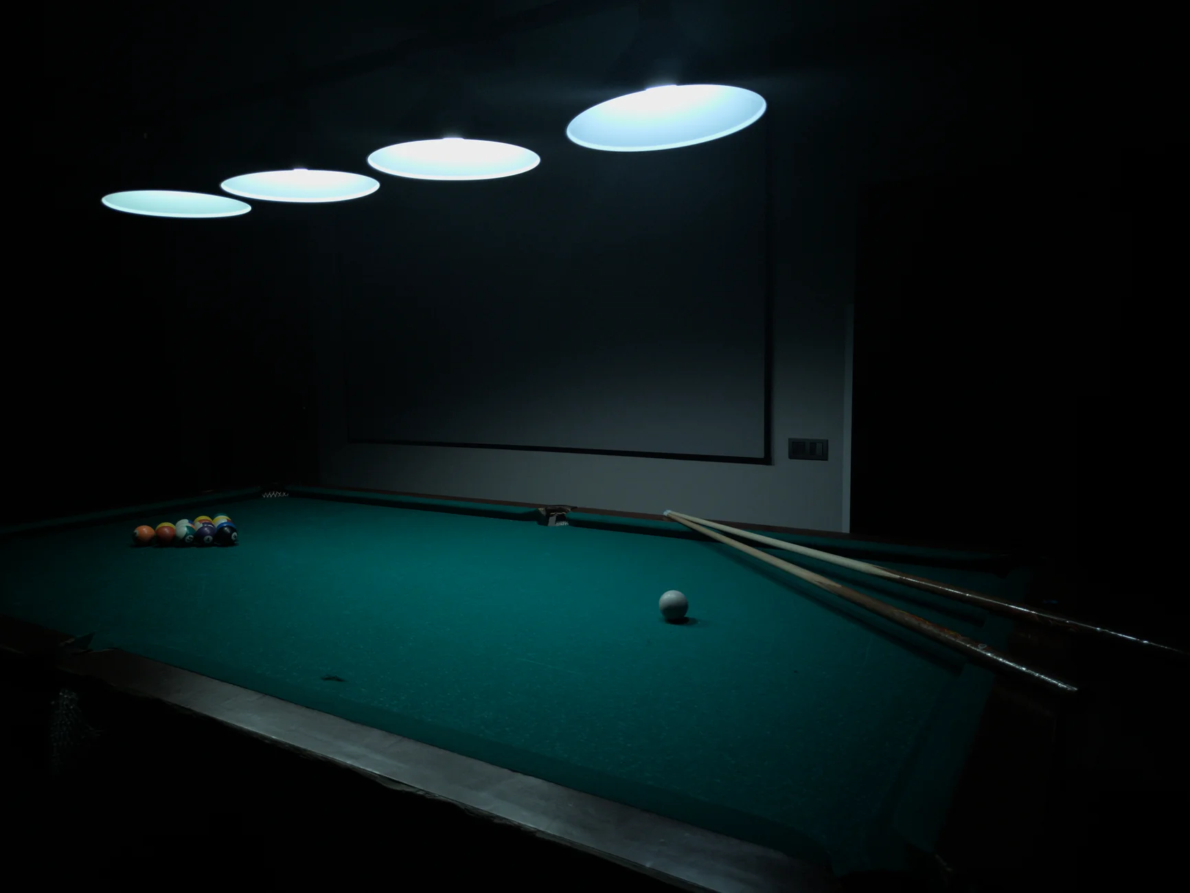 A billiards table under soft lighting with pool balls and cues ready for play.