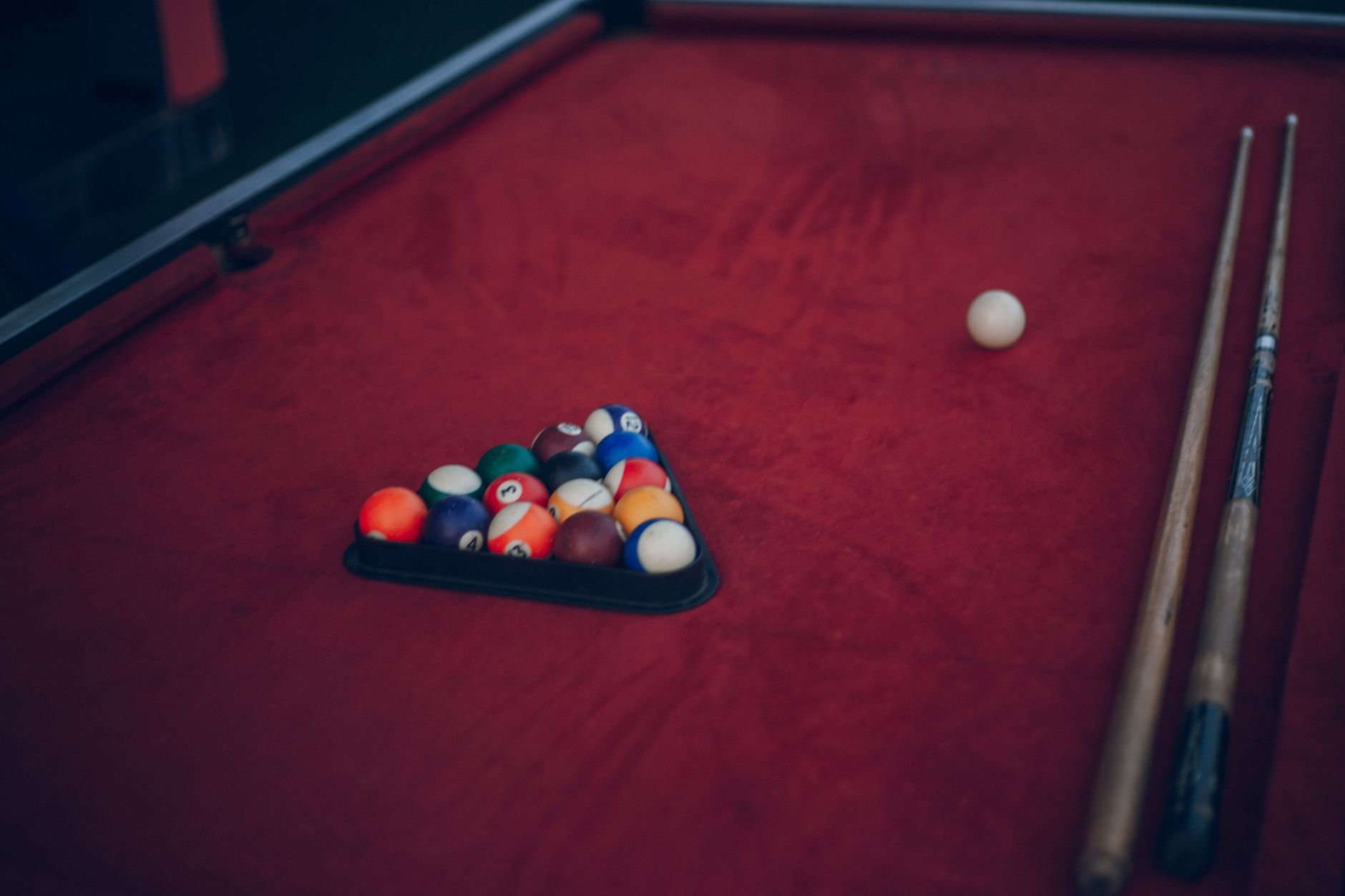 A classic billiard setup with a triangle of pool balls and cues on a red table.